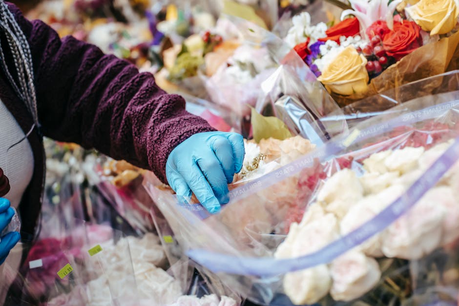 A person wearing a purple textured sleeve and blue disposable gloves is selecting fresh flowers from a large variety of floral arrangements and bouquets, which are wrapped in clear plastic and arrange