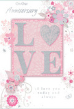 The photograph shows a refined anniversary card whose design seems inspired by a florist's sketchbook, as though prepared for a couple celebrating many shared years in Cricklewood. At its heart, the word LOVE appears prominently in raised, glitter-touched lettering, each character finished in a blend of blush pink and pearly white with delicate silver accents that glisten under the light. The tactile letters invite touch, like tracing the curve of a rose petal. Surrounding this central word is a graceful arrangement of stylized flowers and swirling foliage, all drawn with fine, flowing lines that suggest the airy petals and leaves of springtime bouquets. The blossoms, touched with soft pinks and gentle greys, unfold across a pale blush background, reminiscent of the muted evening sky above nearby Gladstone Park. Slender vines curl between the flowers, introducing gentle movement without clutter, as if the floral motifs are drifting lightly on a breeze. Interwoven with the artwork, elegant scripted messages mark the anniversary occasion and affirm enduring affection, the typography slender and fluid, complementing the curves of the blooms and stems. There are no bold or harsh colours here-only powdery pinks, pearly whites, and subtle silvers that create an atmosphere of intimacy and calm. The card's overall mood is tender and reflective, like a carefully chosen bouquet waiting in a Cricklewood hallway before being handed to a loved one. It feels both contemporary and timeless, a paper keepsake that echoes the artistry and soft romance of a hand-tied floral arrangement.